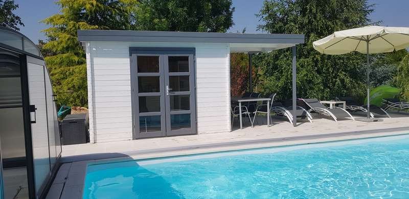 Un abri de jardin blanc se dresse sur une dalle au bord d’une piscine.