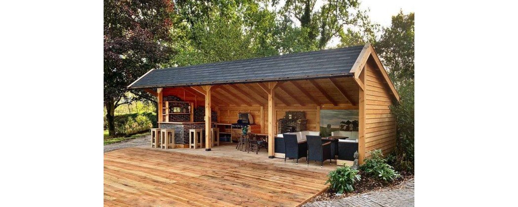 Un abri de jardin en bois abrite une cuisine et un coin salon sur une terrasse en bois.