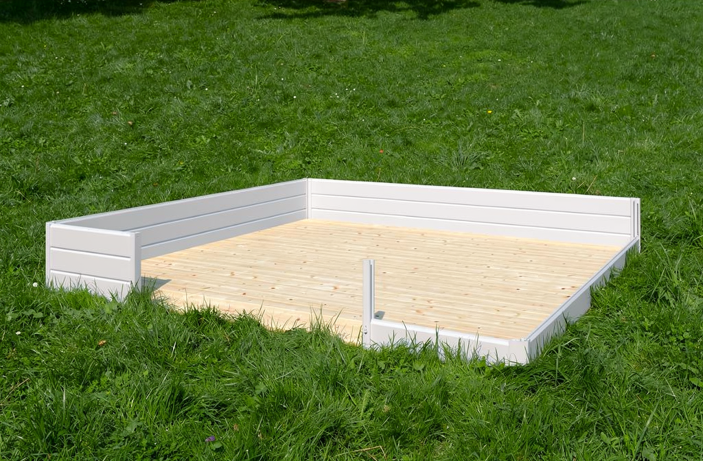 Chalet de jardin habitable 30m2 : plateforme bois entourée de murs blancs surherbée, prête à aménager.