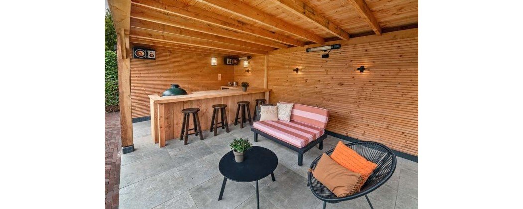 Espace extérieur en bois avec canapé et table basse près d’un bar et de tabourets sous une terrasse bois.