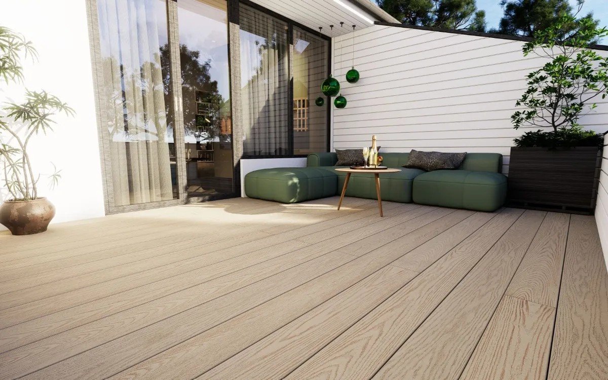 Terrasse extérieure attenante à une roulotte avec canapé d’angle vert et table en bois, entourée de murs blancs et de plantes.